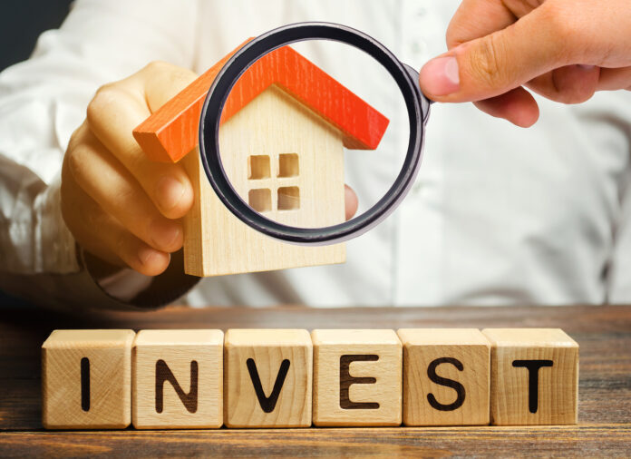 Wooden blocks with the word "Invest" and house in the hands of a businessman.