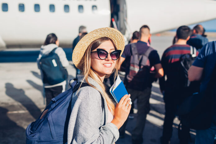 Woman traveler smiling while boarding on plane, holding her passport.